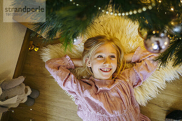 Lächelndes Mädchen  das zu Hause unter dem Weihnachtsbaum liegt
