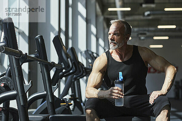 Nachdenklicher reifer Mann mit Wasserflasche im Fitnessstudio