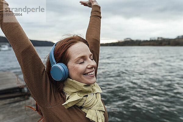 Happy woman with hands raised listening to music by lake