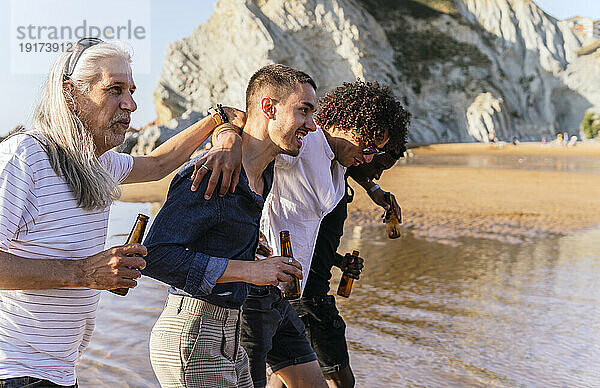 Freunde trinken Bier und spazieren an einem sonnigen Tag gemeinsam am Strand