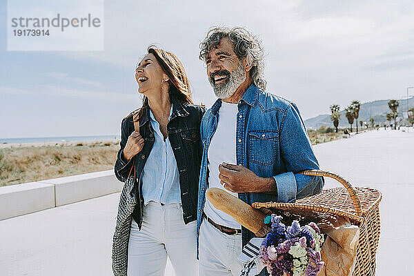 Glückliches älteres Paar mit Picknickkorb in Strandnähe an einem sonnigen Tag