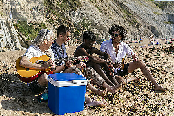 Reifer Mann hält Gitarre und trinkt Bier mit Freunden am Strand
