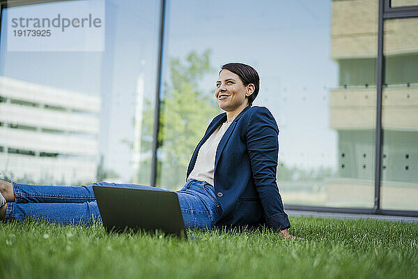 Lächelnde Geschäftsfrau sitzt am Laptop im Gras