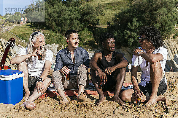 Lächelnde multiethnische Freunde  die im Urlaub gemeinsam Bier am Strand trinken