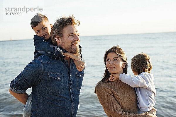 Glückliche Eltern tragen ihre Kinder am Wochenende auf dem Seeweg am Strand