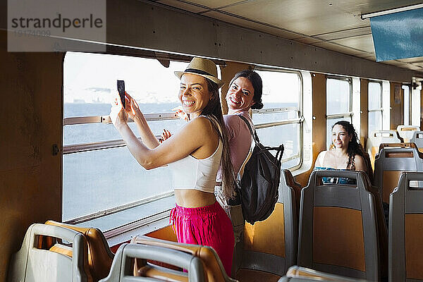 Glückliche Frau hält Smartphone in der Hand und reist mit Freunden im Zug