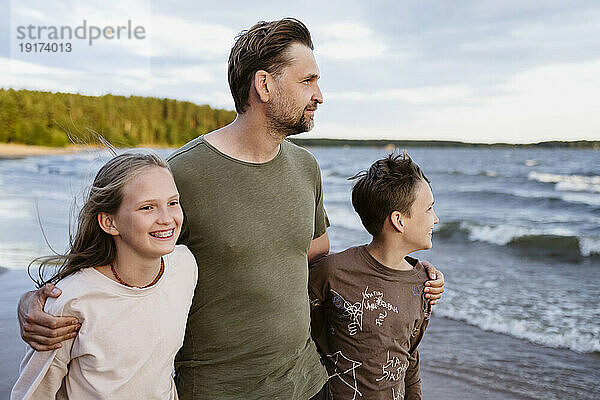 Glücklicher Vater geht mit Sohn und Tochter am Strand spazieren