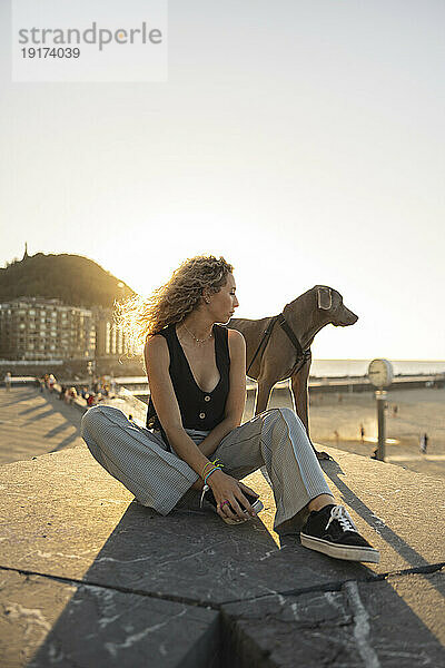 Junge Frau sitzt mit Hund auf der Promenade