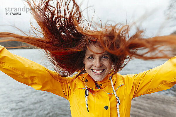 Glückliche rothaarige Frau mit zerzausten Haaren am See