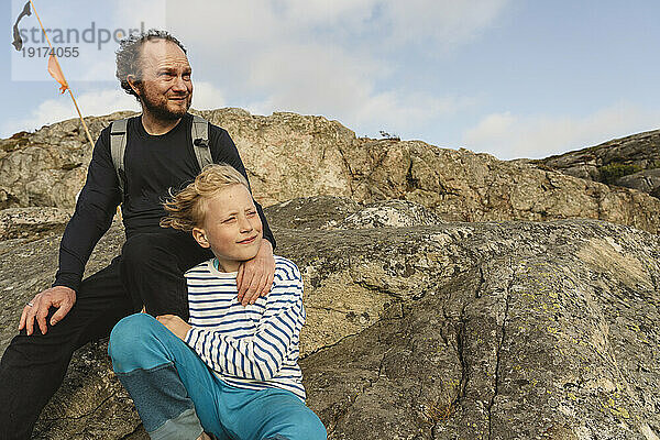 Nachdenklicher Vater und Sohn sitzen zusammen auf einem Felsen