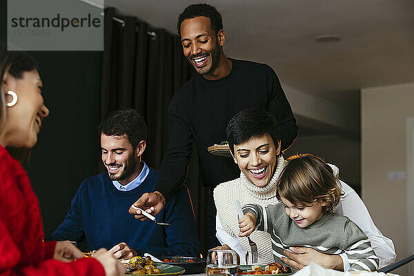 Glücklicher Mann  der der Familie bei einer Dinnerparty an Weihnachten Essen serviert