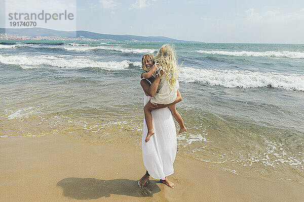 Glückliche Mutter trägt Tochter am Strand