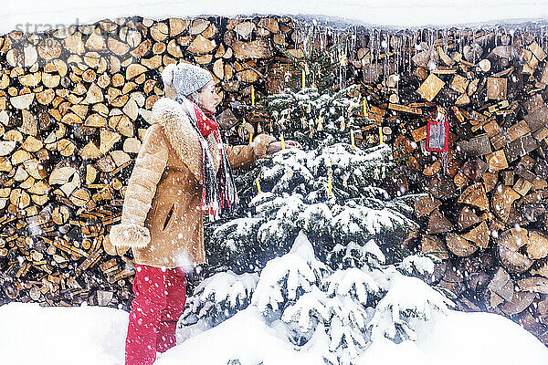 Ältere Frau schmückt Weihnachtsbaum vor Feuerholz