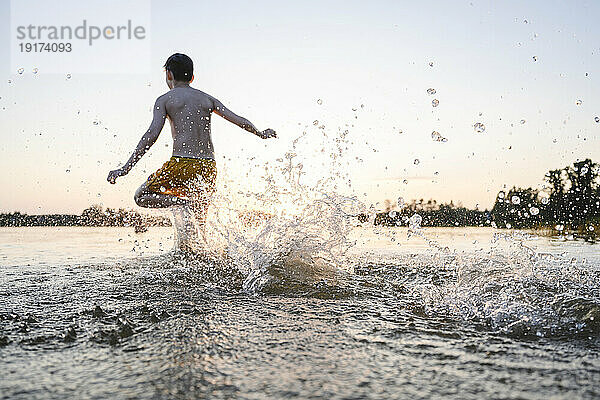 Carefree boy running in lake splashing water
