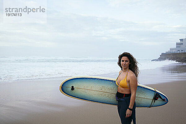 Selbstbewusste junge Frau mit Surfbrett am Strand im Urlaub