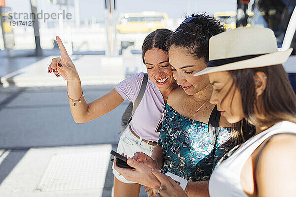 Glückliche Frau gestikuliert an einem sonnigen Tag mit Freunden per Smartphone