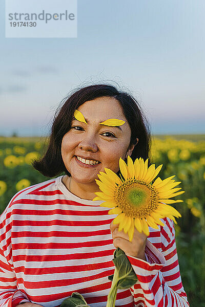 Lächelnde Frau mit Sonnenblumenblättern auf den Augenbrauen im Feld