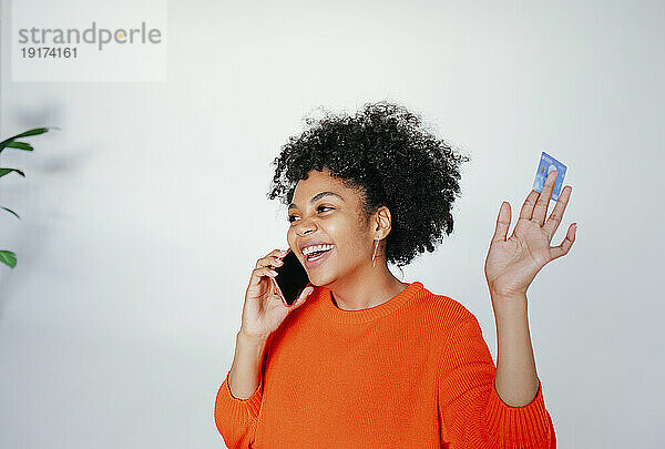 Glückliche Frau mit Kreditkarte  die im Studio mit dem Mobiltelefon spricht