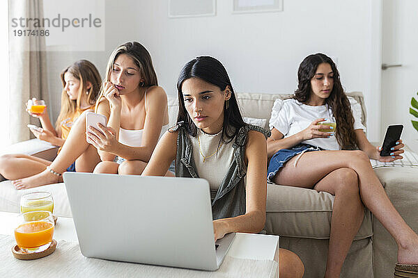 Freunde sitzen zu Hause auf dem Sofa und nutzen Laptop und Smartphone