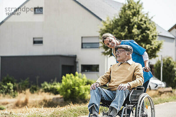 Mitarbeiter im Gesundheitswesen redet und schiebt älteren Mann im Rollstuhl