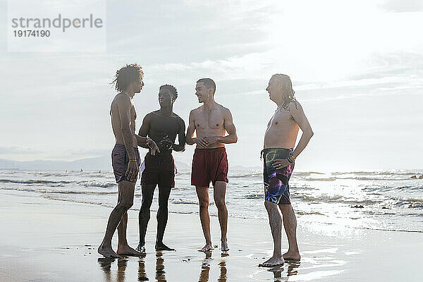 Freunde ohne Hemd stehen an einem sonnigen Tag am Strand