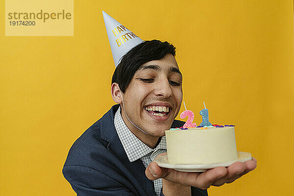 Fröhlicher junger Mann mit Partyhut blickt auf Geburtstagstorte