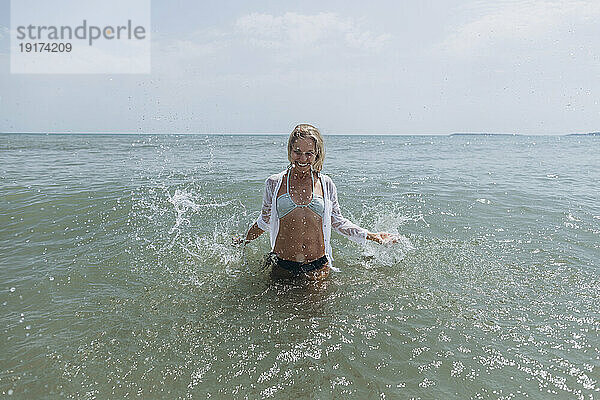 Lächelnde Frau  die Wasser im Meer spritzt