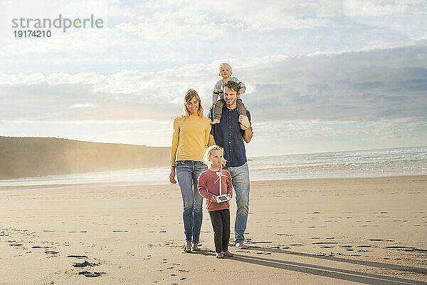 Glücklicher Vater und Mutter  die an einem sonnigen Tag mit Kindern am Meer spazieren gehen