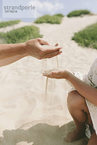 Mutter und Tochter spielen an einem sonnigen Tag mit Sand am Strand