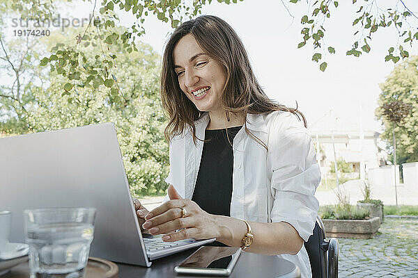 Glückliche Geschäftsfrau benutzt Laptop am Tisch im Garten