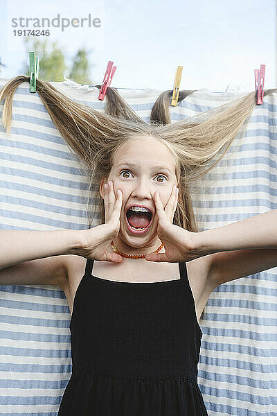 Überraschtes blondes Mädchen mit Haaren in der Wäscheklammer