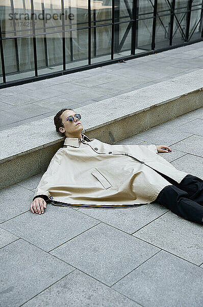 Androgynous man wearing poncho and sleeping on concrete street in city