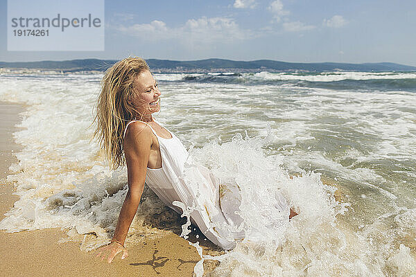 Glückliche Frau sitzt im Wasser am Strand