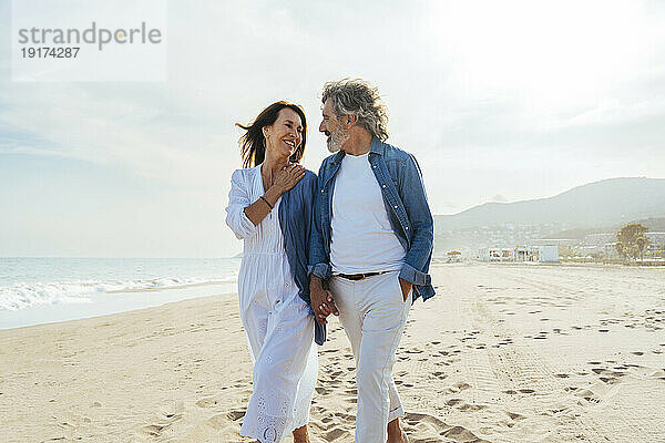 Lächelnder Mann und Frau gehen gemeinsam am Strand spazieren