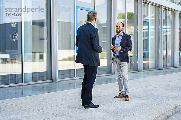 Two businessmen standing in front of office building talking
