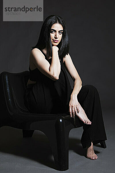 Selbstbewusste schöne Frau sitzt auf einem Stuhl im Studio
