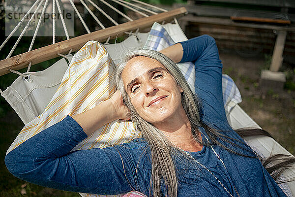 Lächelnde Frau entspannt sich an einem sonnigen Tag in der Hängematte