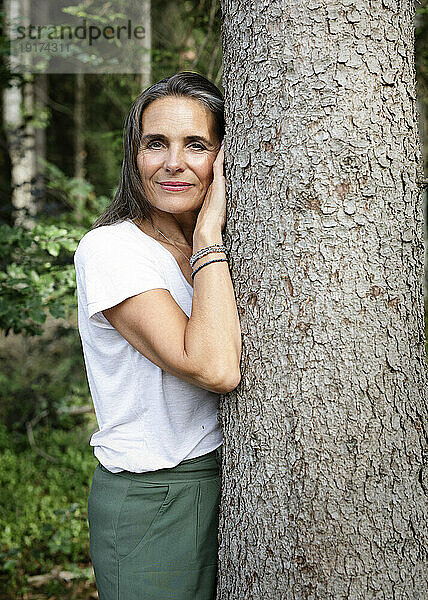 Reife Frau lehnt an Baum im Wald