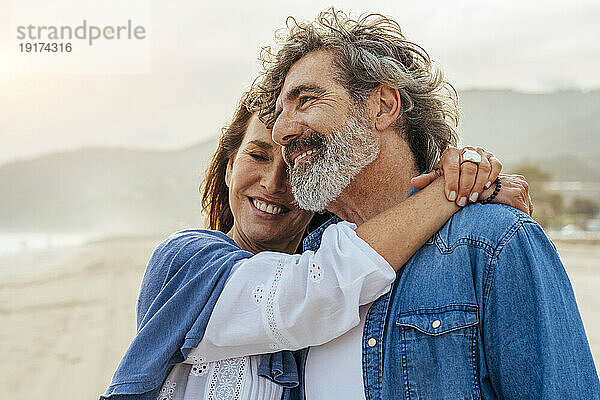 Lächelnde Frau umarmt Mann am Strand