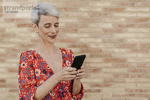 Glückliche Frau benutzt Smartphone vor der Wand