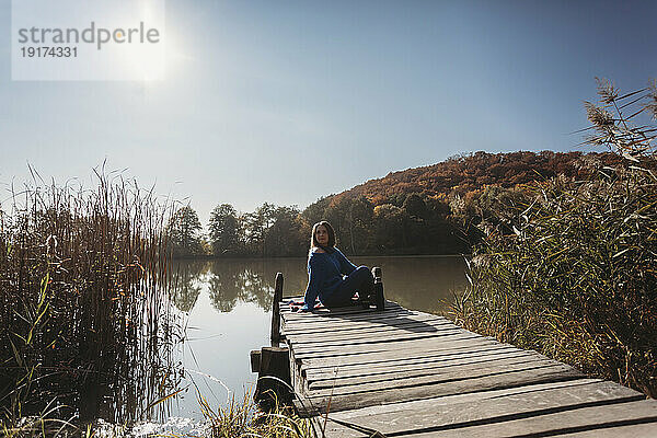 Frau blickt auf die Aussicht  sitzt auf einem Steg in der Nähe des Sees