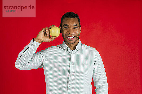 Lächelnder Mann mit Apfel vor rotem Hintergrund