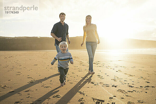 Glücklicher Vater und Mutter spielen mit Sohn am Strand