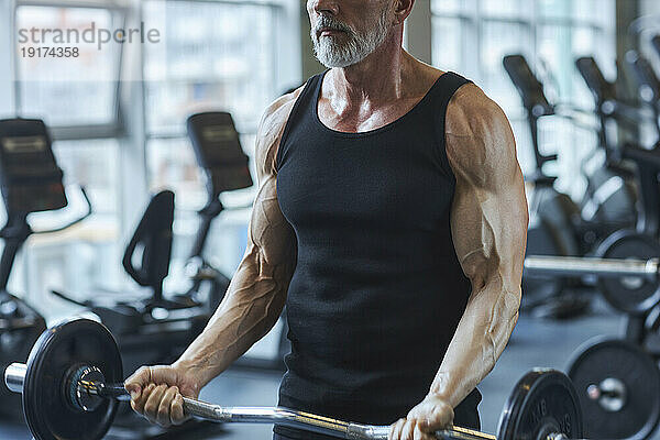 Starker reifer Mann stärkt seine Arme mit der Langhantel im Fitnessstudio