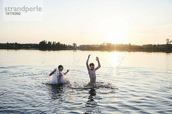 Bruder und Schwester spielen bei Sonnenuntergang im See