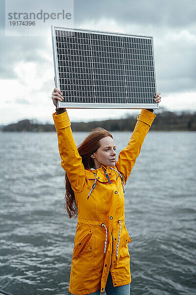 Frau hält Solarpanel vor dem See