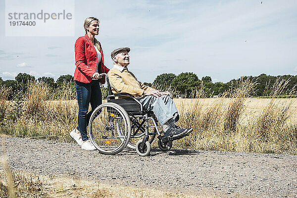 Frau schiebt älteren Mann im Rollstuhl durch Feld