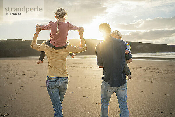 Mutter und Vater gehen mit Kindern am Strand spazieren