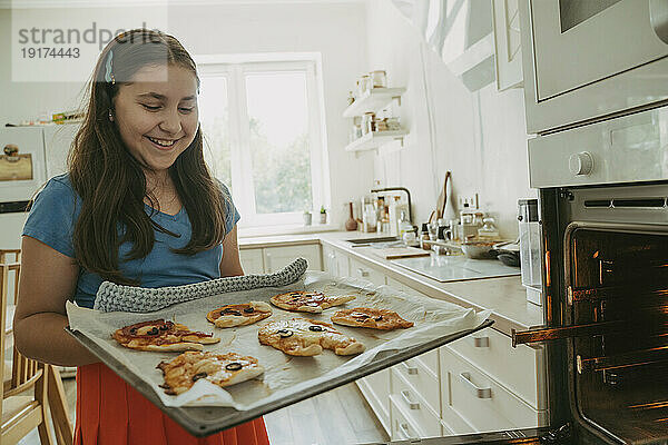 Happy girl holding pizzas on baking tray in kitchen