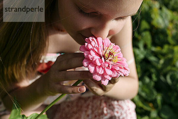 Mädchen hält und riecht rosa Blume im Garten